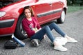 A young girl sitting near a broken car and looking for help, next to her there are bad parts, electric generator, tools and first