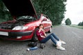 A young girl sitting near a broken car and looking for help, next to her there are bad parts, electric generator, tools and first