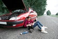 A young girl sitting near a broken car and looking for help, next to her there are bad parts, electric generator, tools and first Royalty Free Stock Photo