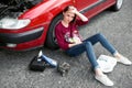 A young girl sitting near a broken car and looking for help, next to her there are bad parts, electric generator, tools and first Royalty Free Stock Photo