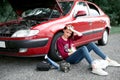 A young girl sitting near a broken car and looking for help, next to her there are bad parts, electric generator, tools and first Royalty Free Stock Photo