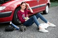 A young girl sitting near a broken car and looking for help, next to her there are bad parts, electric generator, tools and first