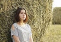 A young girl is sitting near a round stack of straw in a mown field of rye