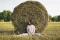 A young girl is sitting near a round stack of straw in a mown field of rye