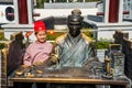 A young girl sitting next to the statue of Acient Chinese Scholar writing on the bable on the bamboo book