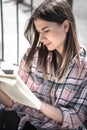 Young girl sitting outside in a plaid shirt and reading a book Royalty Free Stock Photo