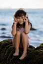 Young girl sitting on the rock near the ocean. Making funny face. Happy childhood. Spending time on the beach. Vacation in Asia. Royalty Free Stock Photo