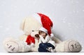 Young girl sitting and sleeping with big soft teddy bear toy in christmas santa red hat under heavy snow Royalty Free Stock Photo