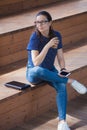 Young girl is sitting on steps, finished work, smiles, checks the phone, drinks coffee. Royalty Free Stock Photo