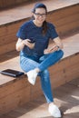 Young girl is sitting on steps, finished work, smiles, checks the phone, drinks coffee. Royalty Free Stock Photo