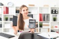 A young girl sitting at a table and holding a phone and a calculator. Royalty Free Stock Photo