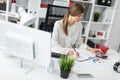 A young girl is sitting at a table in the office, holding a pencil in her hand and counting on a calculator. Royalty Free Stock Photo