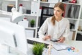 A young girl is sitting at a table in the office, holding a pencil in her hand and counting on a calculator. Royalty Free Stock Photo