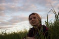 Young girl sitting in tall grass at sunset backlit