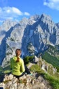 Young girl is sitting on the top of the mountains, enjoying beautiful view on the mountain range Kaisergebirge, Austria. Sunny day Royalty Free Stock Photo