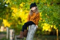 Young girl sitting up the wooden stump and smiling. Autumn background. Copy space Royalty Free Stock Photo