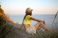 Young girl is sitting on a wild stony sea coast and looking at sea at sunset. Royalty Free Stock Photo