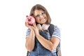 Young girl smiles as she holds her head close to a pink piggybank with savings Royalty Free Stock Photo