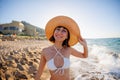 young girl smiling at the camera. Portrait of a beautiful young woman in a straw hat and white bikini on the seashore Royalty Free Stock Photo