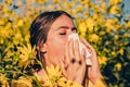 Young girl sneezing and holding paper tissue in one hand and flower bouquet in other. Young woman got nose allergy, flu Royalty Free Stock Photo