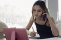 A young girl speaks on the phone, looking at the tablet screen and making notes in a notebook. The concept of freelancing, remote Royalty Free Stock Photo