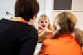 Young girl in speech therapy office. Mirror reflection of young girl exercising correct pronunciation with speech therapist.