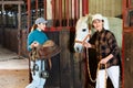 Young girl stable worker ready to saddle horse while Asian woman leading out of stall