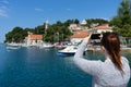 Young girl standing on the coast town taking a photo of adriatic sea with smart phone in Cavtat, Croatia. Red head pony tail