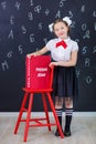 Young girl standing in front of chalkboard brick wall with letters on it wearing school uniform with huge pensil yellow color