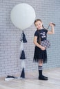 Young girl standing in front of chalkboard brick wall with letters on it wearing school uniform with huge pensil yellow color