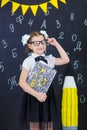 Young girl standing in front of chalkboard brick wall with letters on it wearing school uniform with huge pensil yellow color