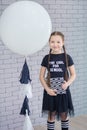 Young girl standing in front of chalkboard brick wall with letters on it wearing school uniform with huge pensil yellow color