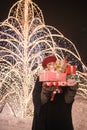 Young girl standing in front of Christmas tree lights hiding behind presents Royalty Free Stock Photo