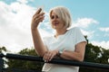 A young girl is standing outdoors in a park and talking on the phone, smiling. Girl against the sky Royalty Free Stock Photo