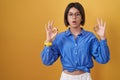Young girl standing over yellow background looking surprised and shocked doing ok approval symbol with fingers Royalty Free Stock Photo