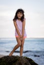 Young girl standing on the rock near the ocean and smiling. Happy childhood. Spending time on the beach. Cute little girl. Summer Royalty Free Stock Photo