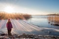 Young girl standing at a shore looking at winter sunset with sun flares.