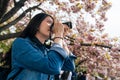 Young girl standing under sakura tree in the park in spring. beautiful woman professional photographer love hobby taking photo of