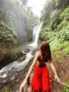Young girl standing by the waterfall surrounded by greenery.