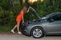 A young girl stands at a broken car and looks at the engine, does not understand how to repair Royalty Free Stock Photo