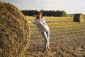 A young girl stands near a round stack of straw on a mown field of rye