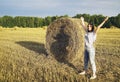 A young girl stands near a round stack of straw on a mown field of rye