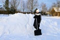 young girl stands with shovel at large pile of snow in countryside. Teenage girl helps adults clean up snow. Royalty Free Stock Photo