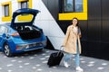 A young girl stopped to charge her electric car, and in the meantime goes to rest, carrying a suitcase Royalty Free Stock Photo