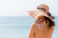 Young girl in straw hat is applying sunscreen on her back to protect her skin