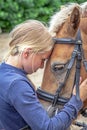 A young girl strokes her pony and speaks sweet words to the horse.