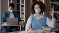 Young girl student in medical mask sits at desk in library preparing to lesson writing note in notebook looks at camera Royalty Free Stock Photo