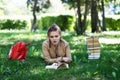 Young girl student reading a book lying on grass in the park.