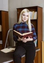 Young girl student standing and reading book near bookshelves in library background Royalty Free Stock Photo