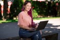 Young girl is studying in the spring park, sitting on the wooden bench and browsing on her laptop Royalty Free Stock Photo